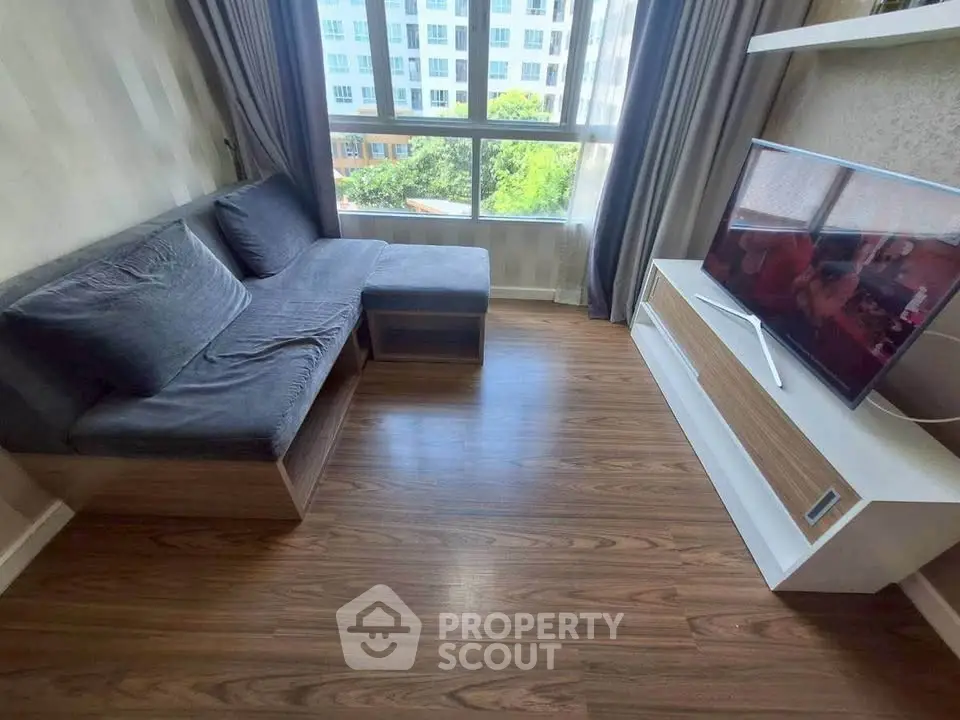 Cozy living room with modern sofa and flat-screen TV, featuring large window with natural light.