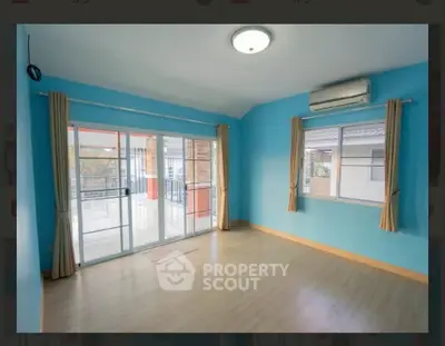 Spacious empty room with large windows and balcony access, featuring blue walls and wooden flooring.