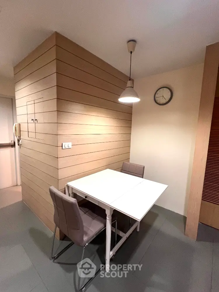 Modern dining area with sleek table and chairs, stylish lighting, and wall clock in cozy apartment.