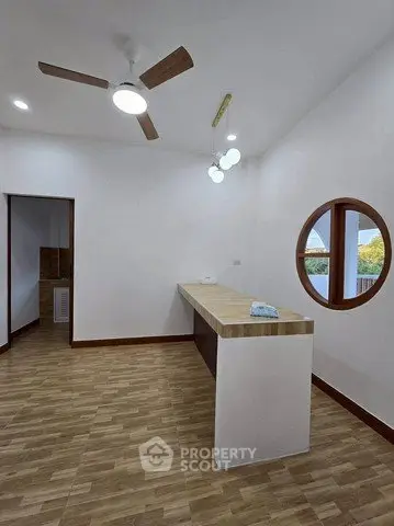 Modern kitchen with wooden flooring and round window, featuring a sleek countertop and ceiling fan.