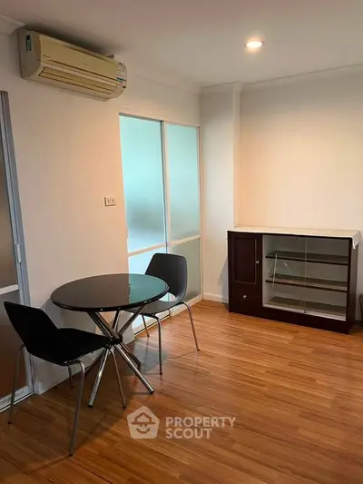 Modern living room with sleek furniture and wooden flooring, featuring a compact dining area and air conditioning.