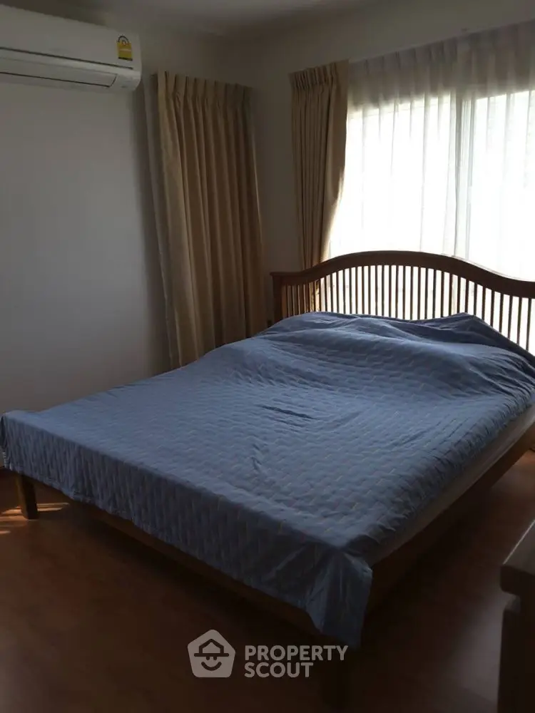 Cozy bedroom with wooden bed frame and natural light from large window.
