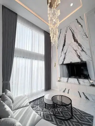 Luxurious living room with high ceilings, elegant chandelier, and marble accent wall.