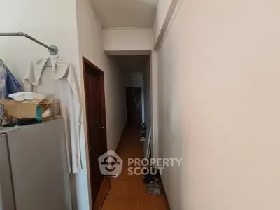 Narrow hallway with tiled floor and wooden door, showcasing compact living space.