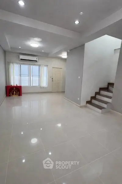 Spacious modern living room with glossy tiled floors and staircase, perfect for family gatherings.