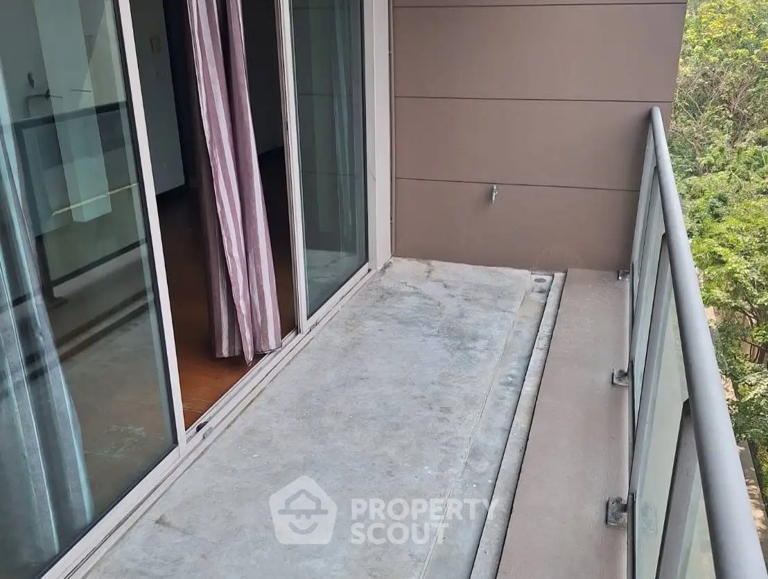 Spacious balcony with glass railing and sliding doors overlooking greenery