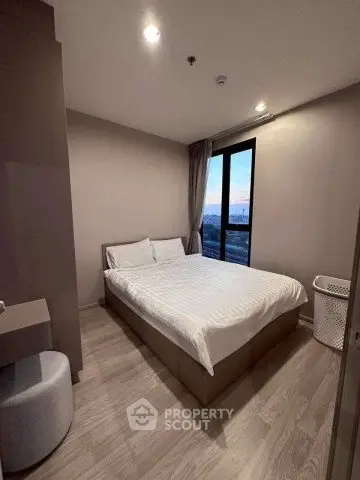 Cozy bedroom with modern decor and large window offering city views.