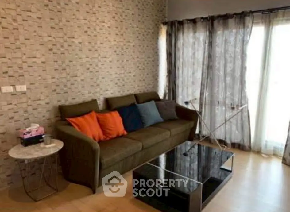 Cozy living room with modern sofa and glass coffee table, featuring textured wall and natural light.