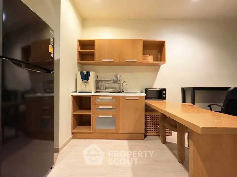 Modern compact kitchen with wooden cabinets and sleek appliances in cozy apartment.