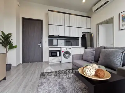Modern living room with integrated kitchen featuring washing machine and sleek cabinetry.