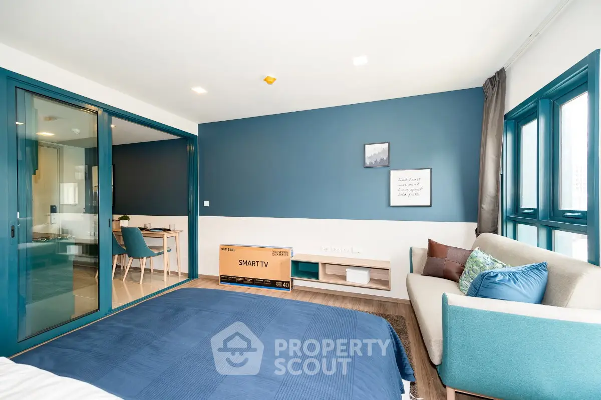 Modern bedroom with blue accents, smart TV, and cozy seating area in a stylish apartment.