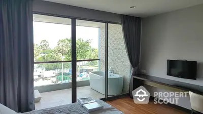 Modern bedroom with balcony and outdoor bathtub overlooking lush greenery.