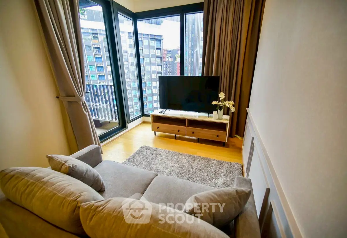 Modern living room with large windows and city view, featuring cozy sofa and TV setup.