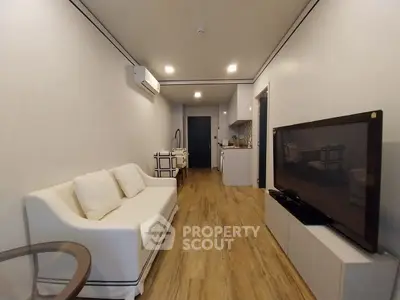 Modern living room with sleek design, featuring a cozy sofa, large TV, and compact kitchen area.