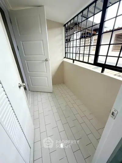 Bright enclosed balcony with tiled floor and large windows in modern apartment.