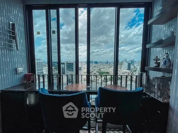 Stunning city view from a modern high-rise balcony with seating area.