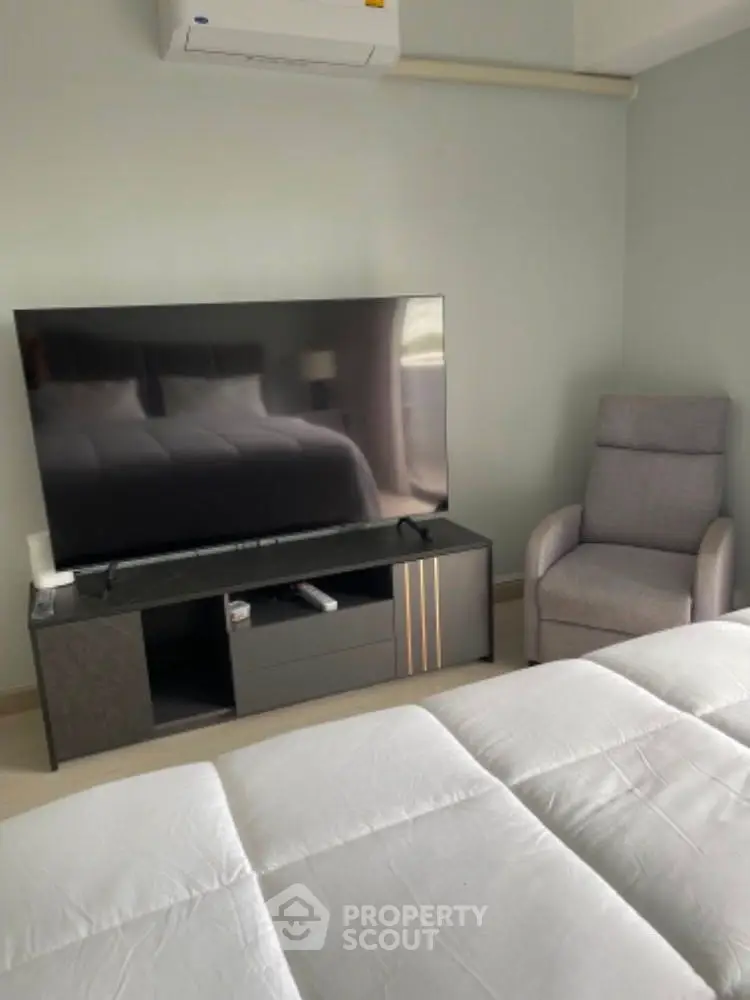 Cozy bedroom with modern TV setup and comfortable armchair, perfect for relaxation.