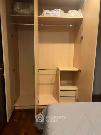 Spacious wooden wardrobe with open shelves and hanging space in a cozy bedroom setting.