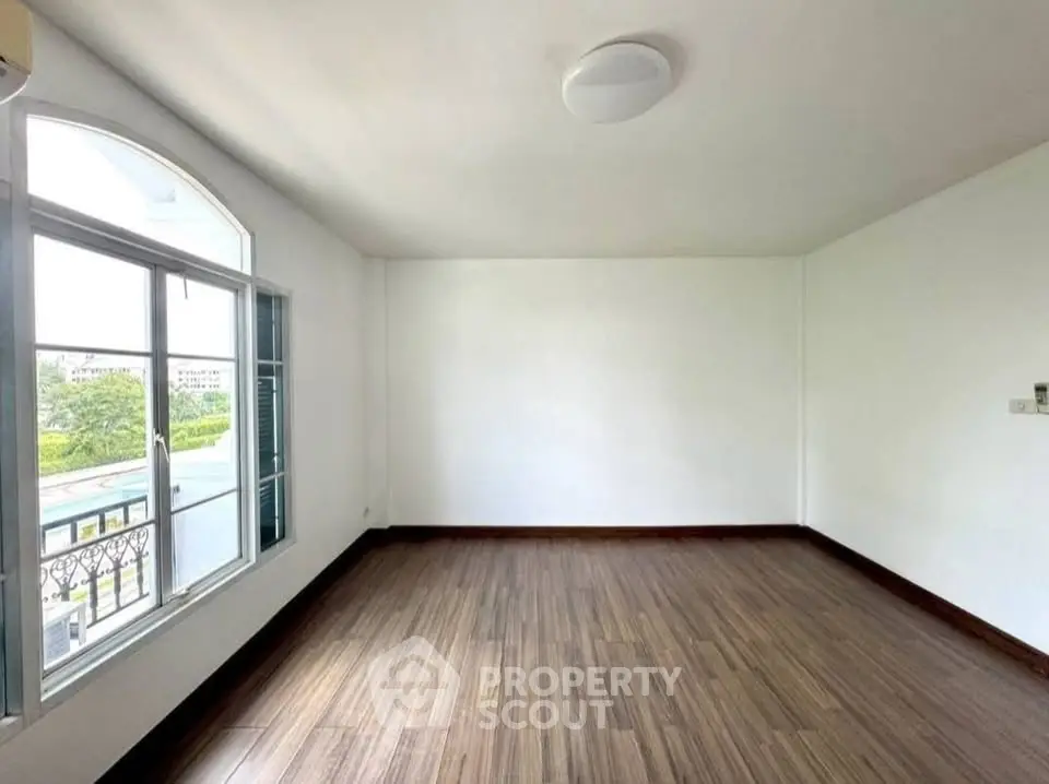 Spacious empty room with large window and wooden flooring, perfect for customization.