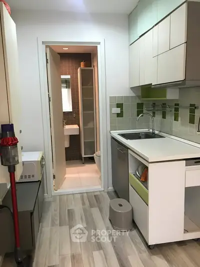 Modern compact kitchen with sleek cabinetry and open layout leading to a small bathroom.