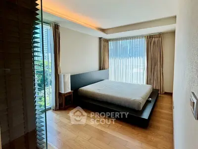 Modern bedroom with large windows and wooden flooring, offering a serene city view.