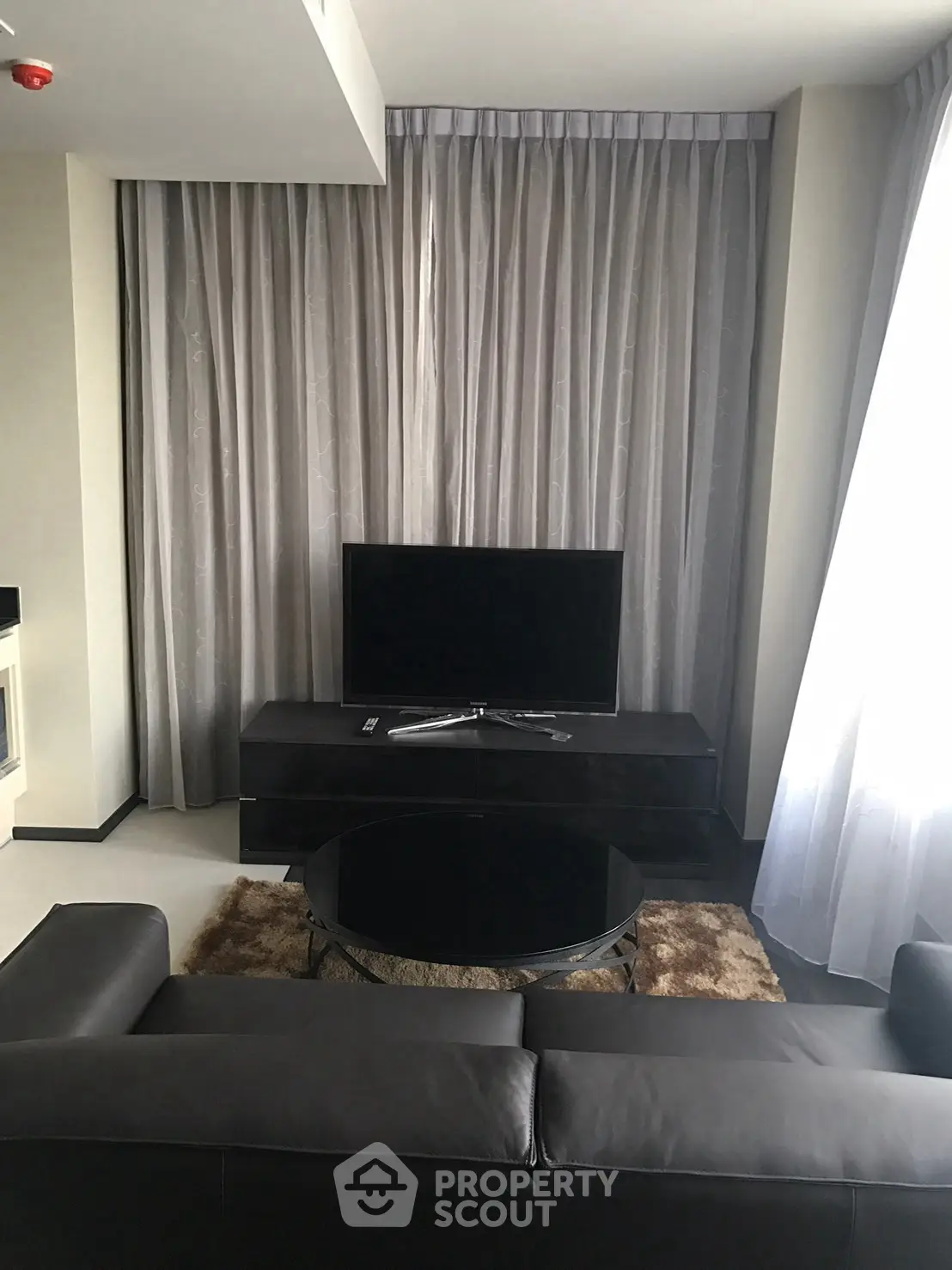Modern living room with sleek black furniture and large TV, elegant curtains enhance the ambiance.