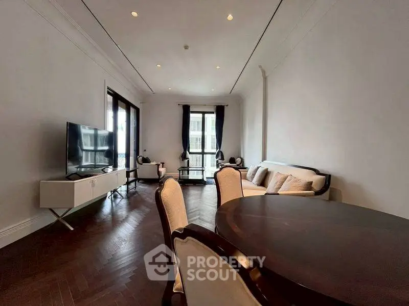 Elegant living room with dark wood flooring and modern furniture, featuring a large TV and ample natural light.