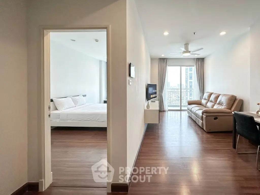 Spacious modern apartment with open living room and bedroom, featuring sleek wooden flooring and natural light.