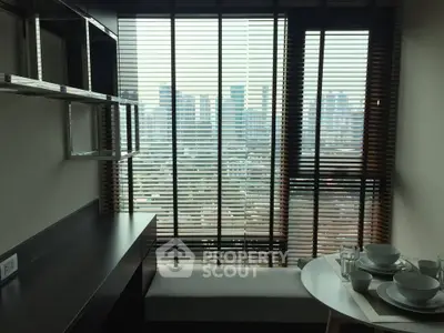 Modern apartment with city view, featuring sleek furniture and large windows with blinds.