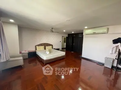 Spacious bedroom with polished hardwood floors, large bed, and modern air conditioning unit, offering a blend of comfort and luxury.
