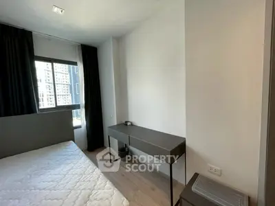 Modern bedroom with sleek furniture and large window offering city views.