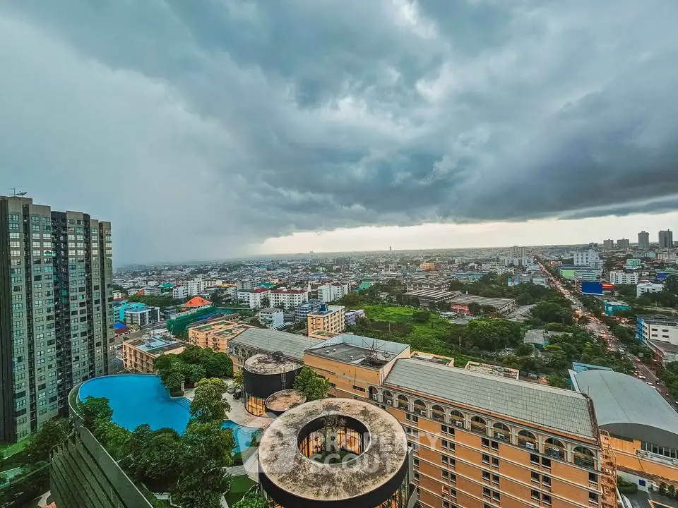 Stunning cityscape view from high-rise building with dramatic clouds and lush greenery.