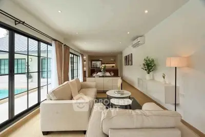 Spacious living room with modern decor and poolside view, featuring large windows and elegant furniture.