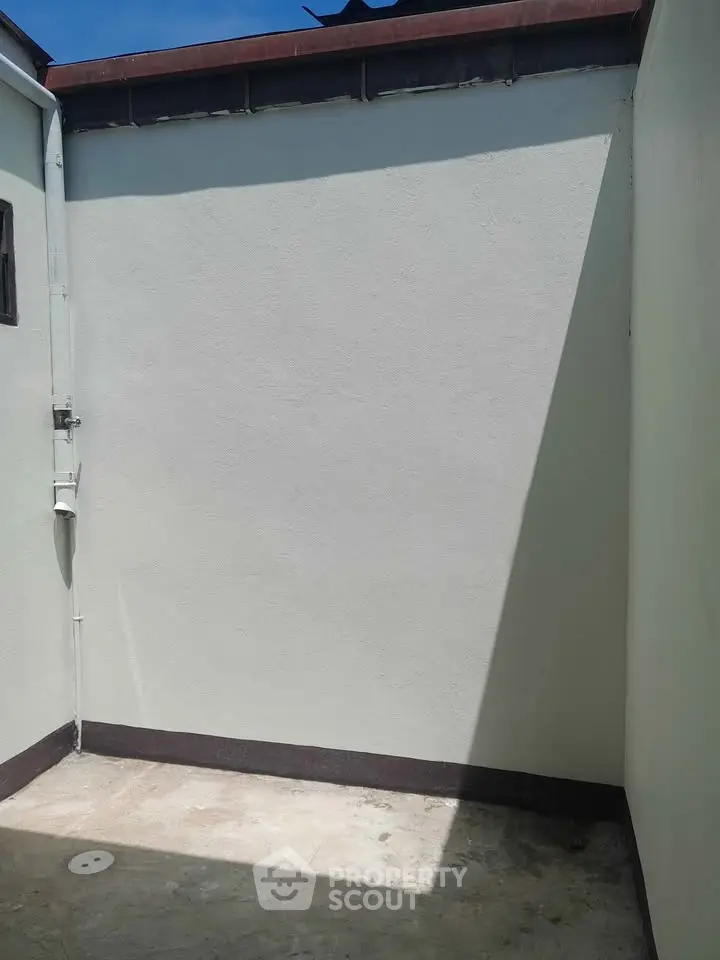 Minimalist outdoor space with clean white walls and concrete floor, perfect for customization.