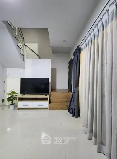 Spacious modern living room with sleek staircase and large TV, perfect for family gatherings.