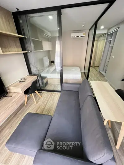 Modern studio apartment with glass partition, stylish furniture, and wooden flooring.