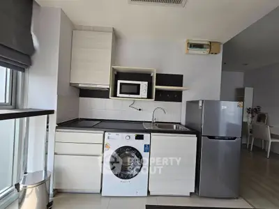 Modern kitchen with washing machine, microwave, and fridge in a compact open layout.