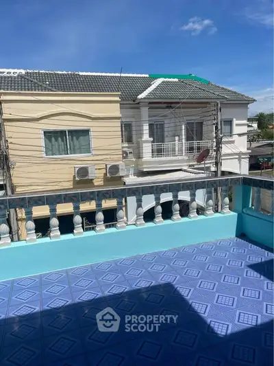 Spacious balcony with blue tiled flooring and view of neighboring houses under clear sky.