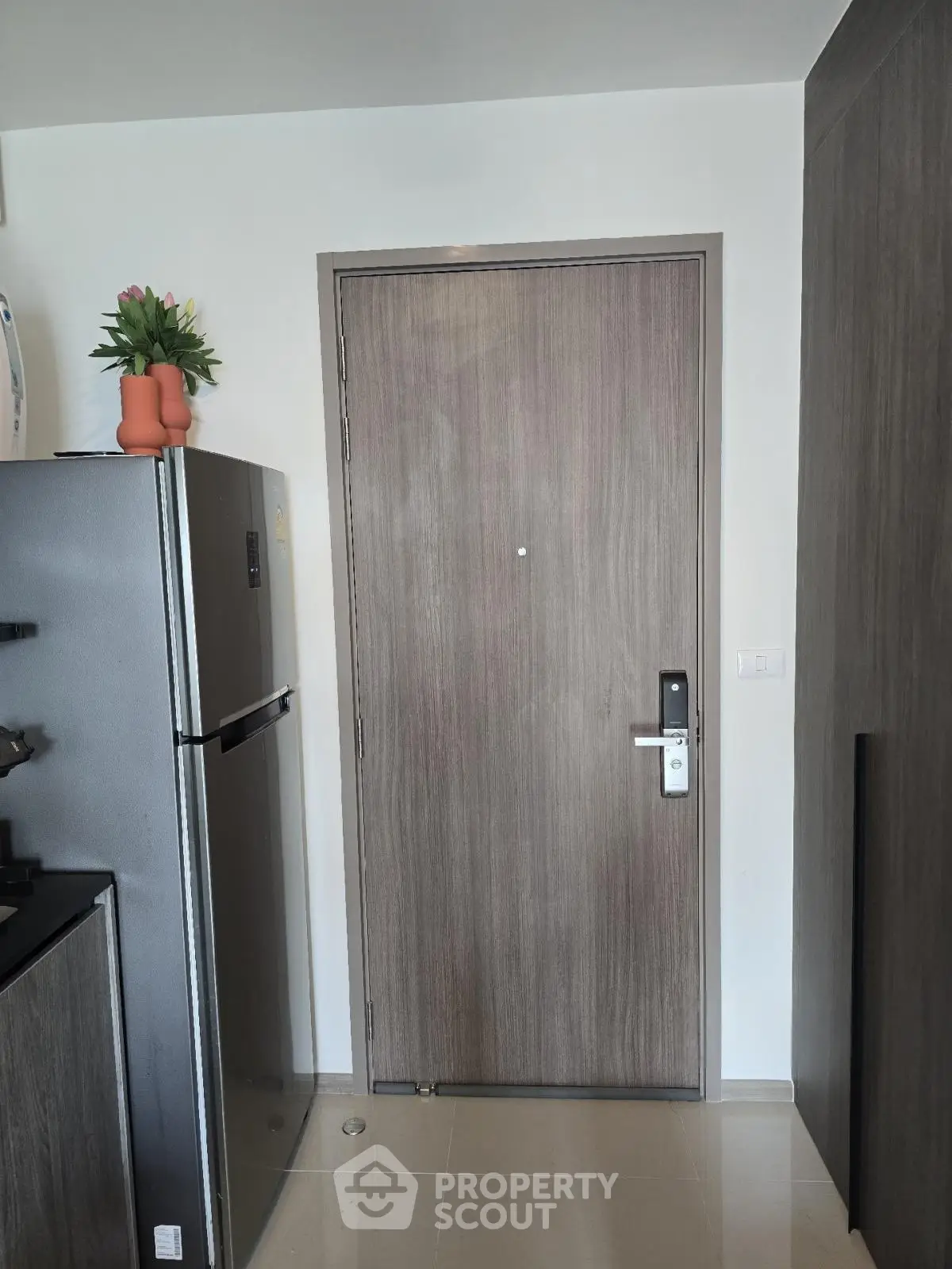 Modern apartment entrance with sleek wooden door and stainless steel fridge