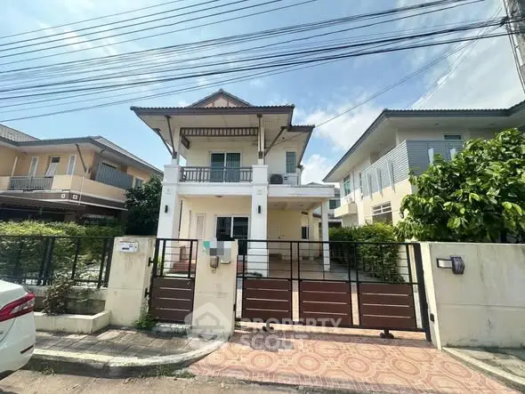 Charming two-story house with balcony and gated entrance in a serene neighborhood.