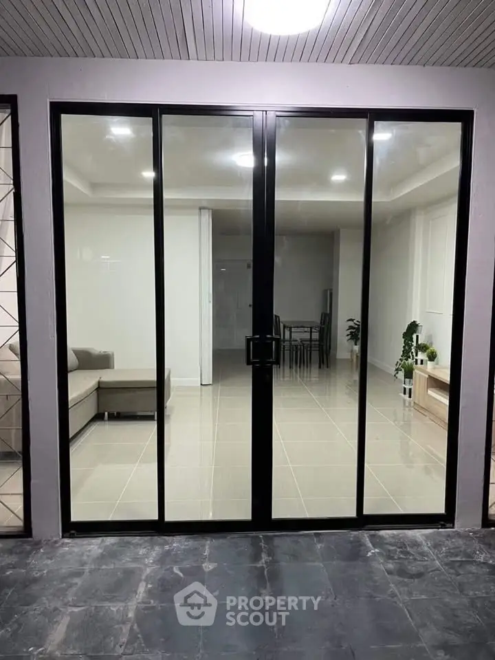 Modern interior view through glass doors with sleek furniture and tiled flooring.