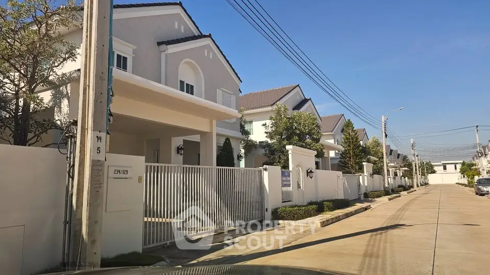 Charming suburban street with modern detached houses and lush greenery under clear blue skies.