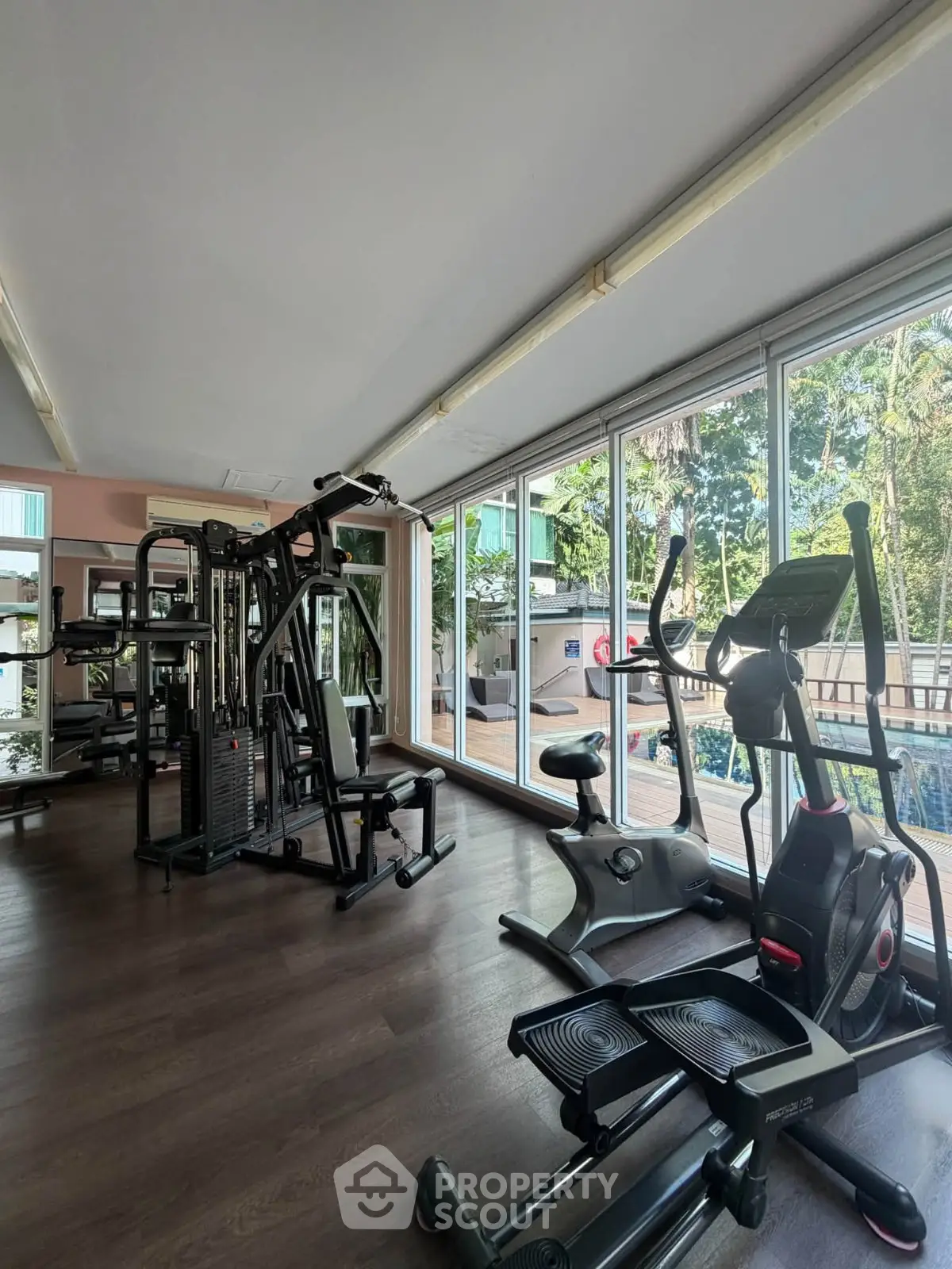 Spacious gym with modern equipment and large windows overlooking lush greenery.