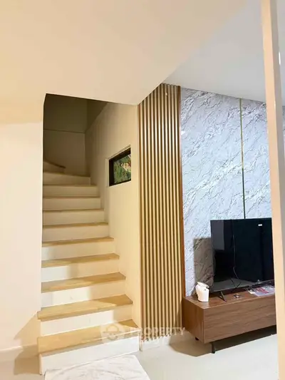 Modern living room with stylish staircase and TV unit, featuring elegant wall paneling.
