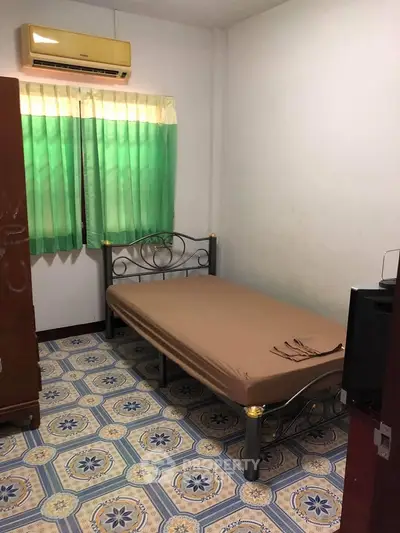 Cozy bedroom with metal bed frame and patterned tile flooring, featuring a window with green curtains.