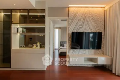 Modern living room with sleek TV setup and view into a stylish bedroom, featuring elegant wood flooring.