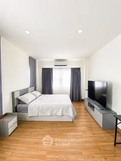Spacious modern bedroom with wooden flooring and large TV, perfect for relaxation.