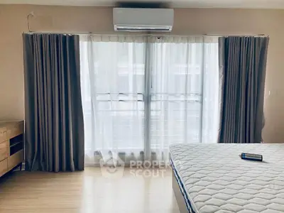 Spacious bedroom with large window and air conditioning, featuring modern curtains and a comfortable mattress.