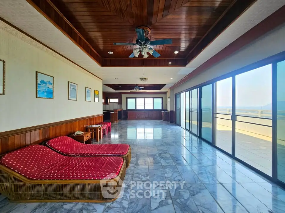 Spacious living room with large windows and stunning view, featuring elegant wooden ceiling and marble flooring.