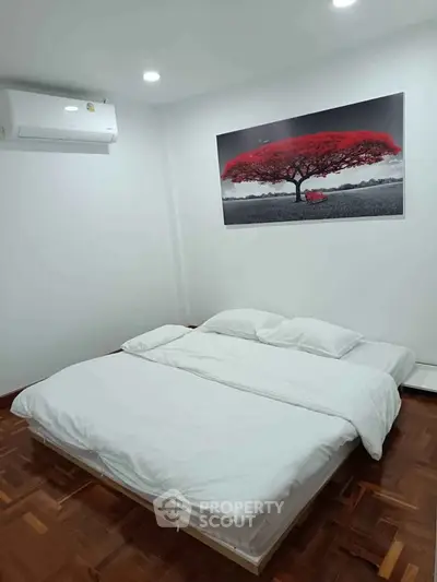Minimalist bedroom with modern art and wooden flooring, featuring a cozy bed and air conditioning.